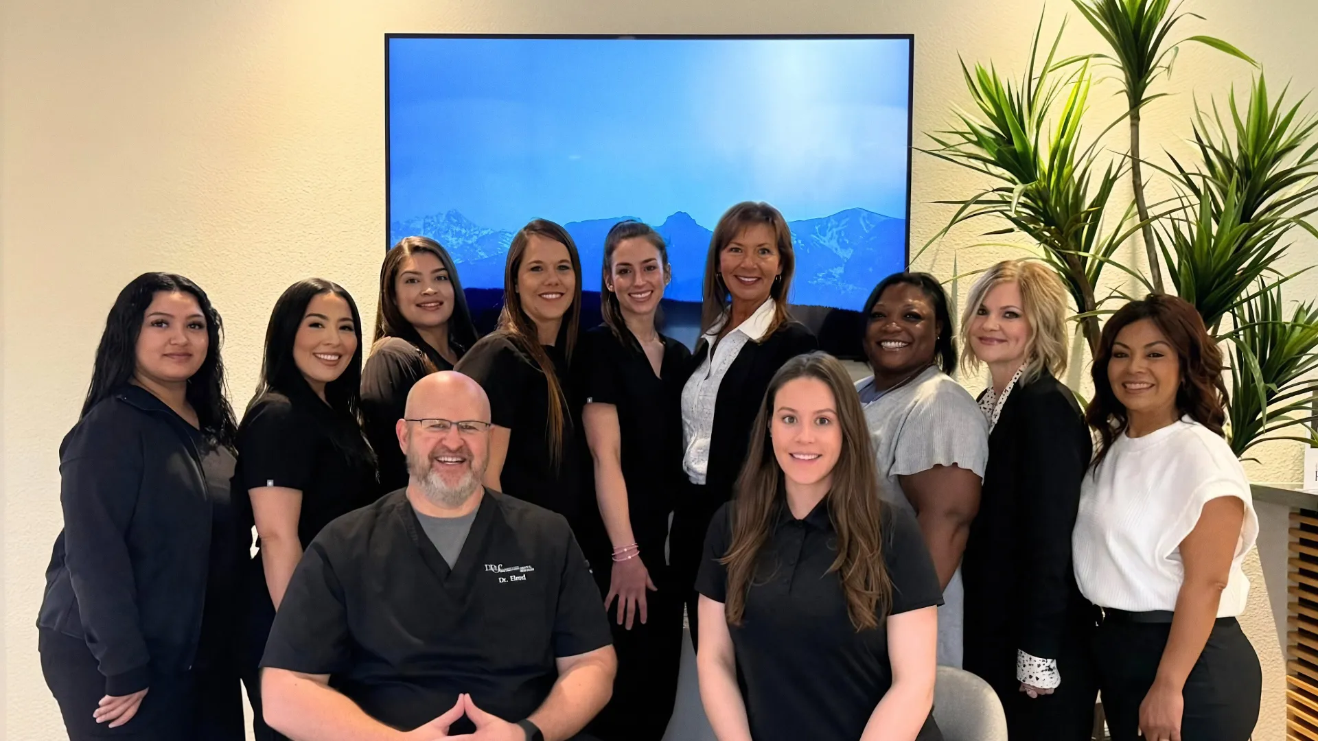 Group portrait of diverse medical team in black scrubs and professional attire smiling in modern office.