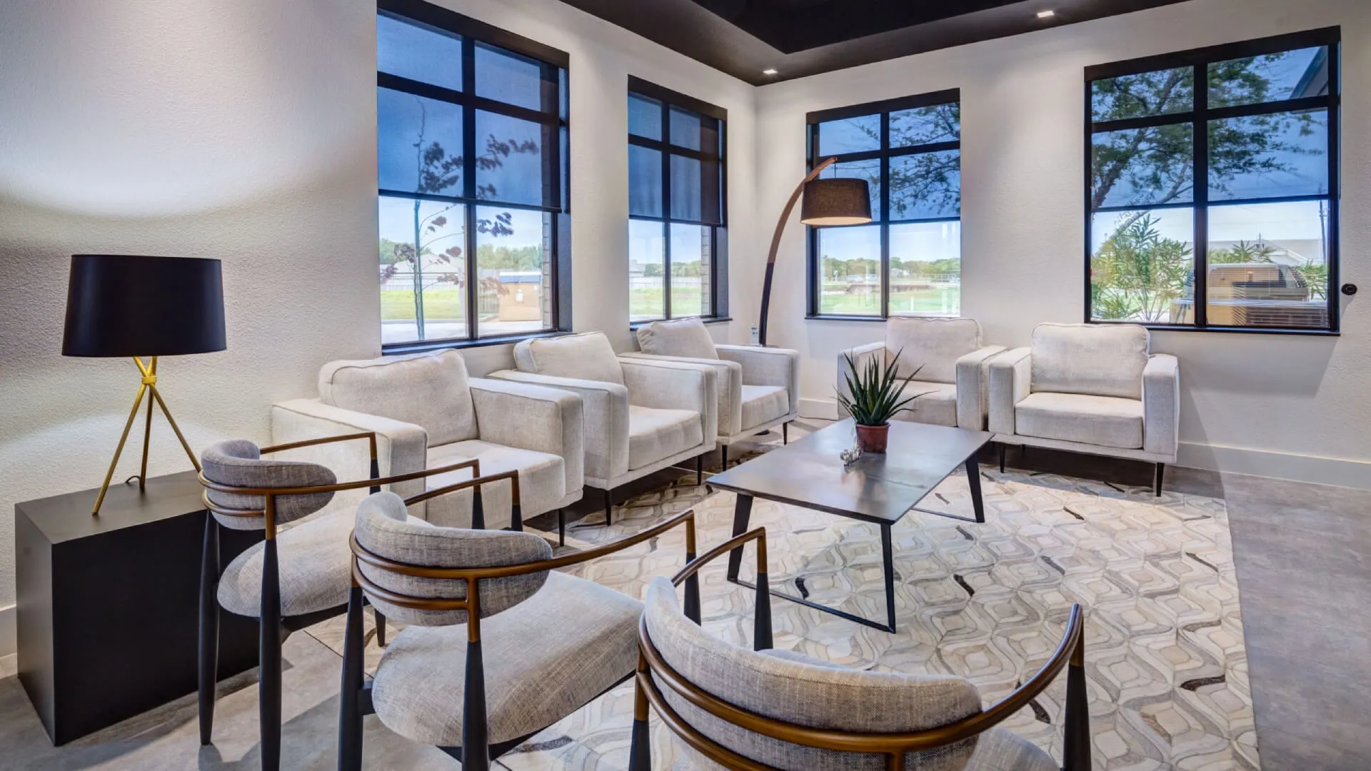 Modern living room with gray armchairs, large windows, a geometric rug, and minimalist decor including a potted plant.