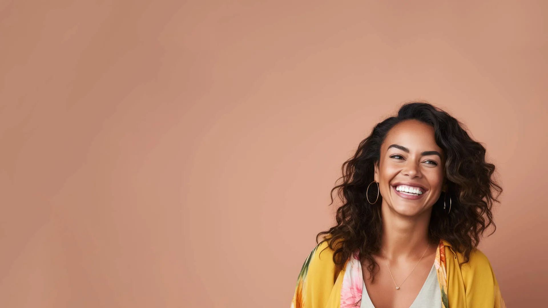 Smiling woman with curly hair wearing yellow floral jacket against peach background