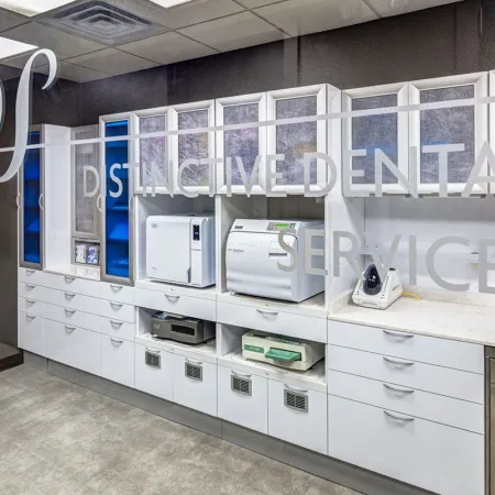 Modern dental lab with white cabinets, sterilization equipment, and clean gray flooring behind glass door.
