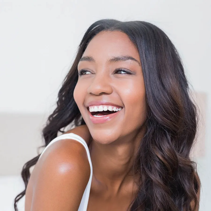 Smiling young woman with long wavy hair looking to the side in bright natural light indoors.