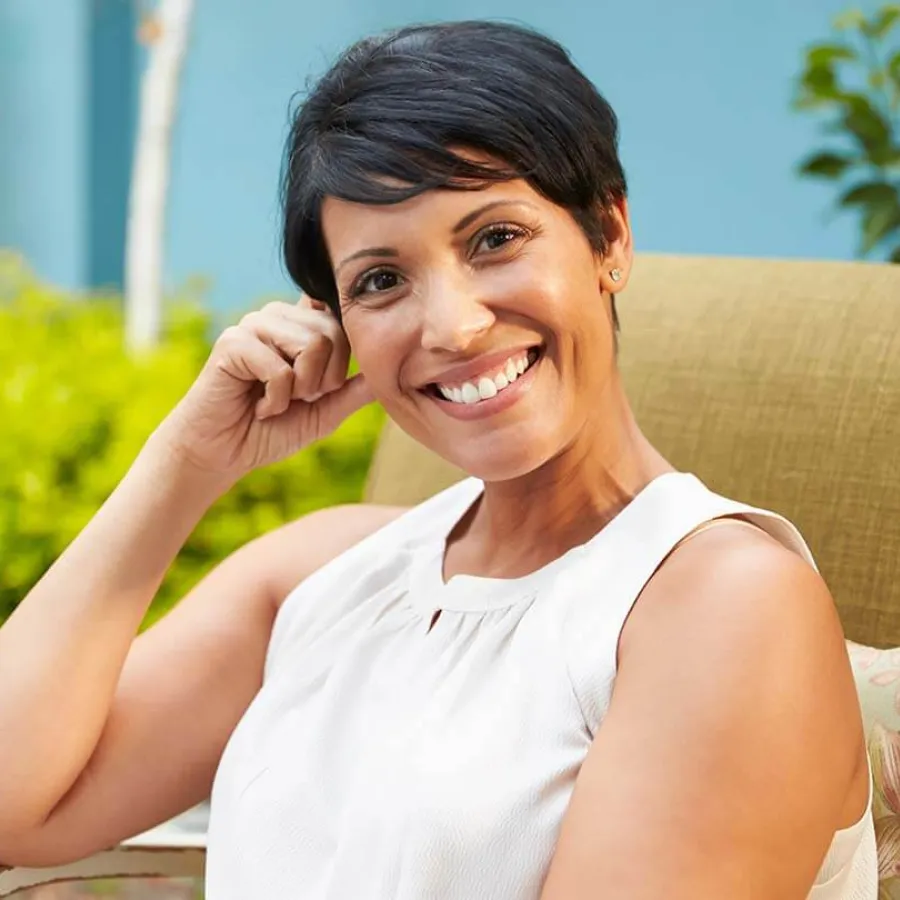 Smiling woman with short hair relaxing in a sunny garden setting on a cozy chair.