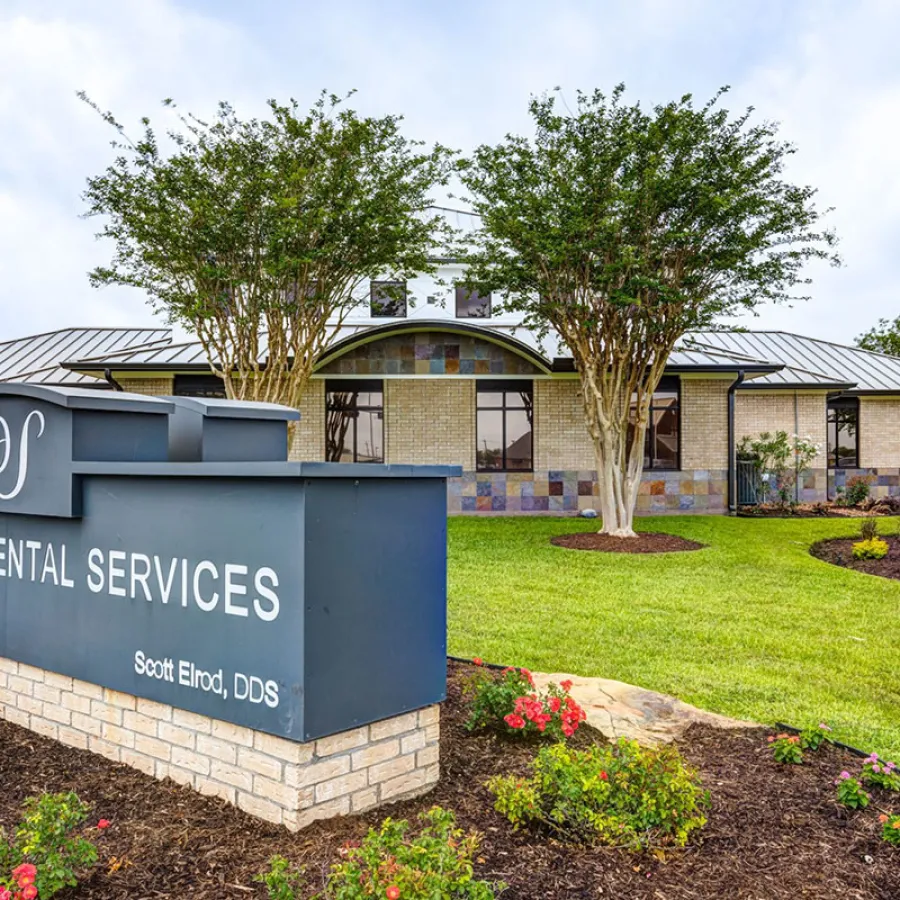 Modern dental office building with landscaped garden and Distinctive Dental Services sign in front on a cloudy day