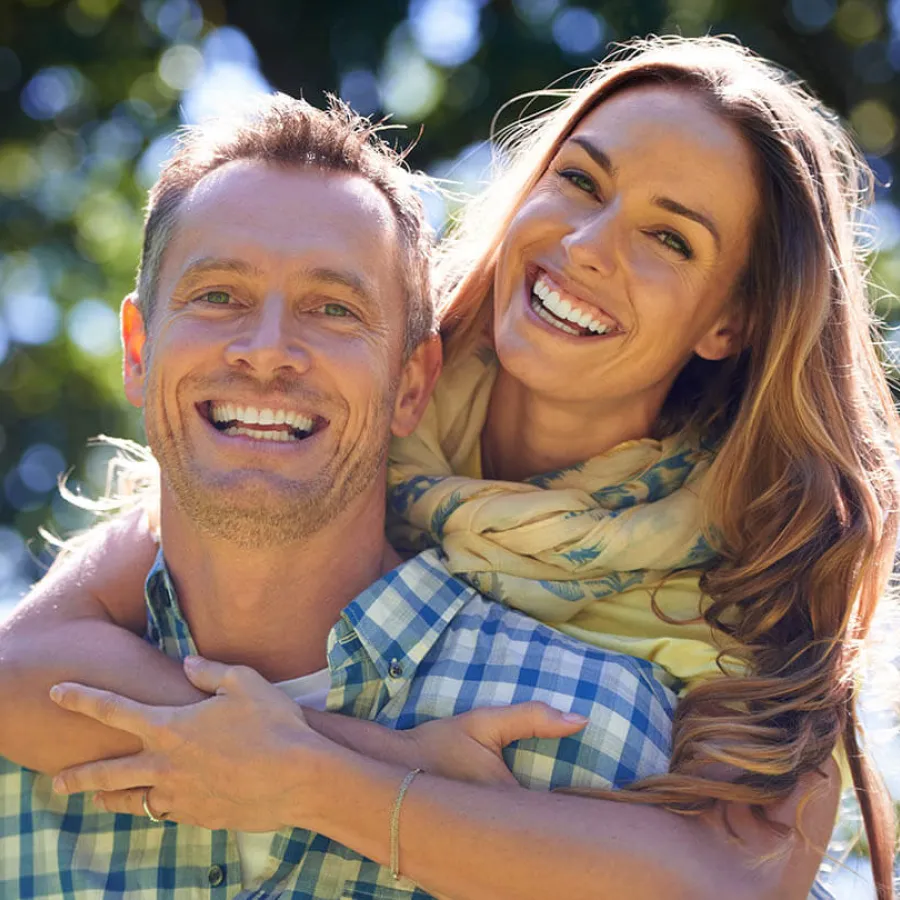A joyful couple smiling together outdoors, showcasing happiness and connection in a sunny environment.