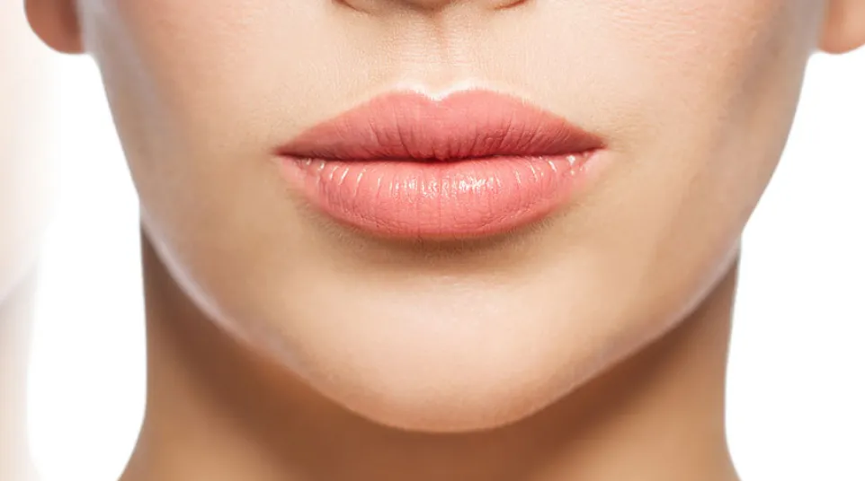 Close-up of a woman's smooth lips and lower face with natural, soft pink lipstick and clear skin.